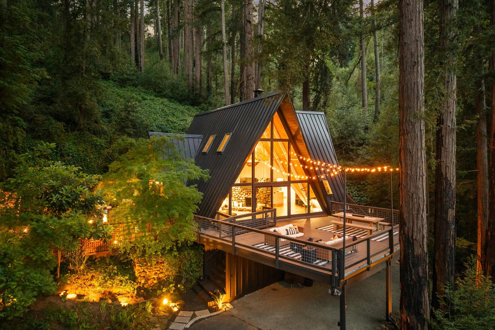 Aerial view of Summit House A-frame glowing at twilight, nestled among ancient redwoods on Mount Veeder